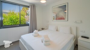 Een moderne hotelkamer met een groot bed, een plafondventilator, een raam met uitzicht op groen en een schilderij aan de muur.