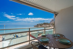 A balcony with a table set for dining, overlooking a beach and ocean.