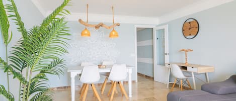 A dining area with a table and chairs, a plant, and a wall clock.