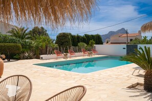 A swimming pool with a tiled deck, surrounded by palm trees and red chairs.