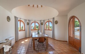 A dining area with a wooden table and chairs, surrounded by arched windows with curtains, and a tiled floor. - CostaBlancaDreams - Casa Julo in Calpe (Calpe)