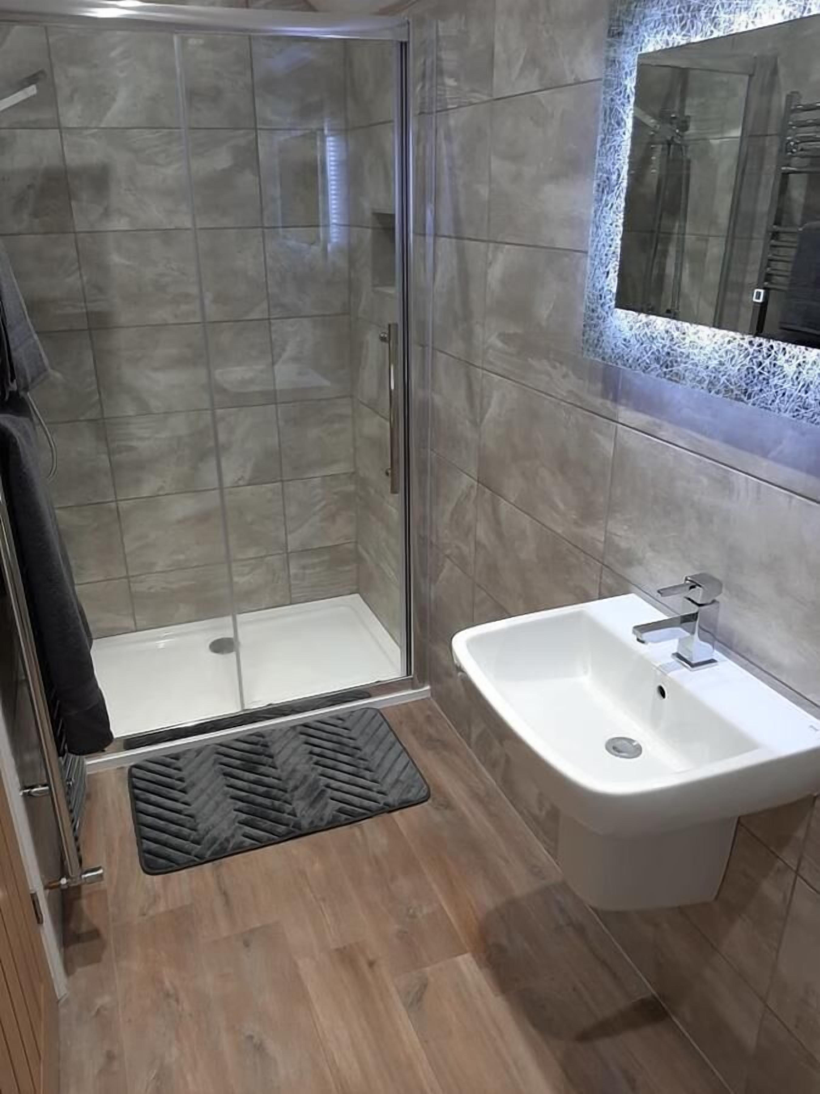 Un baño moderno con ducha de vidrio, lavamanos blanco y suelo de madera.