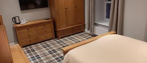 A bedroom with a bed, a wooden wardrobe, a television on the wall, and a window with curtains.