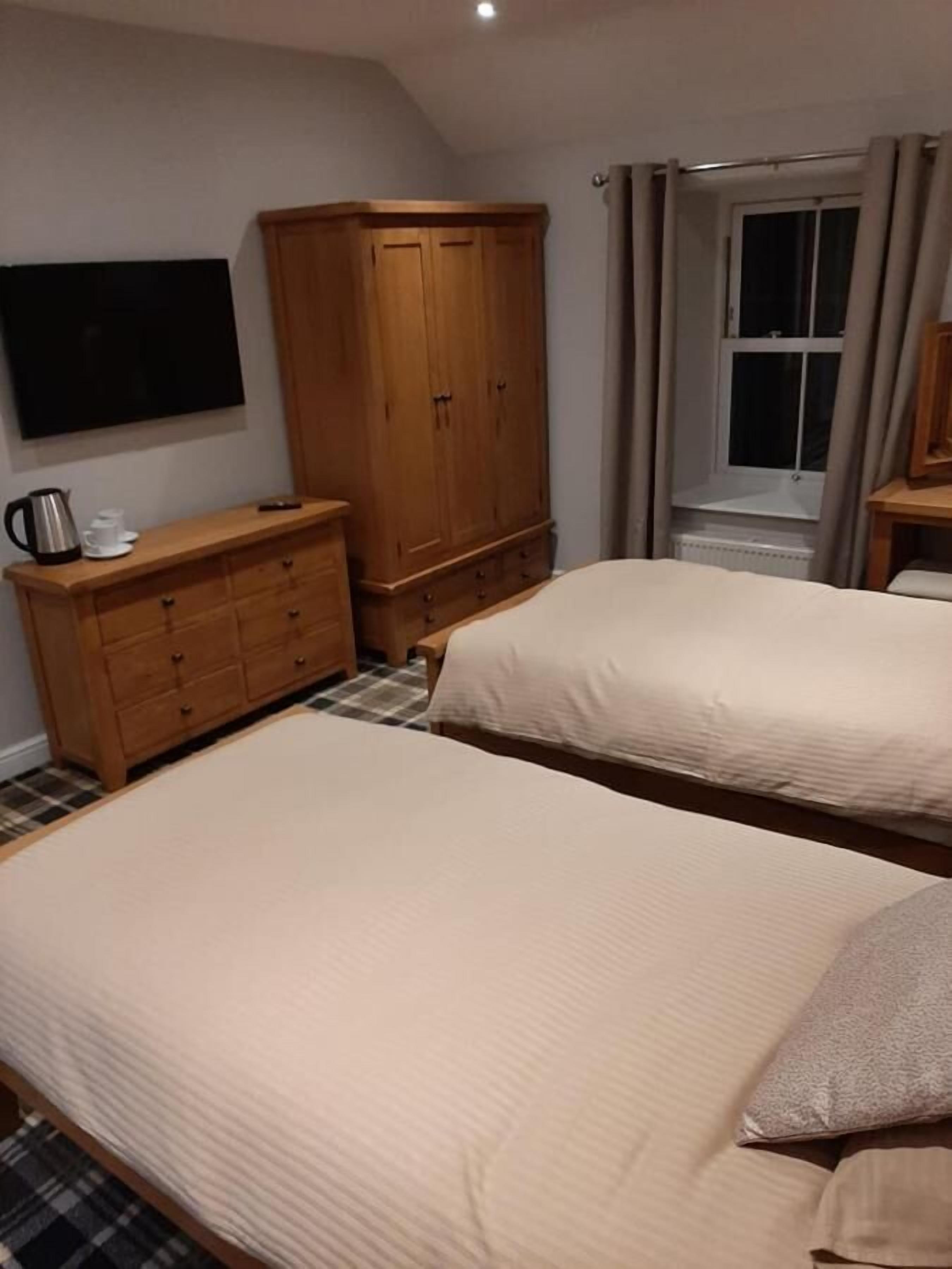 Een slaapkamer met twee bedden, een houten garderobe, een aan de muur bevestigde televisie en een raam met gordijnen.