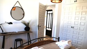 Una camera d'albergo con un letto, una scrivania con lampada, una sedia e uno specchio a parete. Ci sono degli asciugamani sul letto e una porta con maniglia nera.