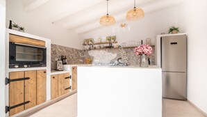 Una cucina moderna con mobili in legno, forno integrato, frigorifero in acciaio inossidabile e illuminazione a sospensione.