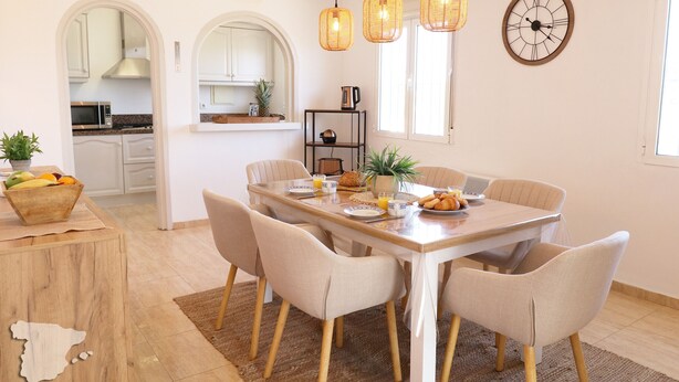 Un'area pranzo con un tavolo in legno, sedie color beige e una sveglia appesa al muro.