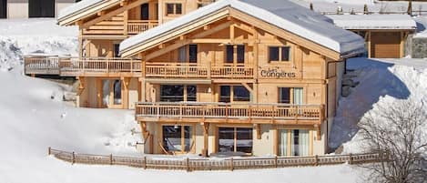 Un chalet en bois doté de balcons, une enseigne indiquant « Les Congrès », et un paysage enneigé.