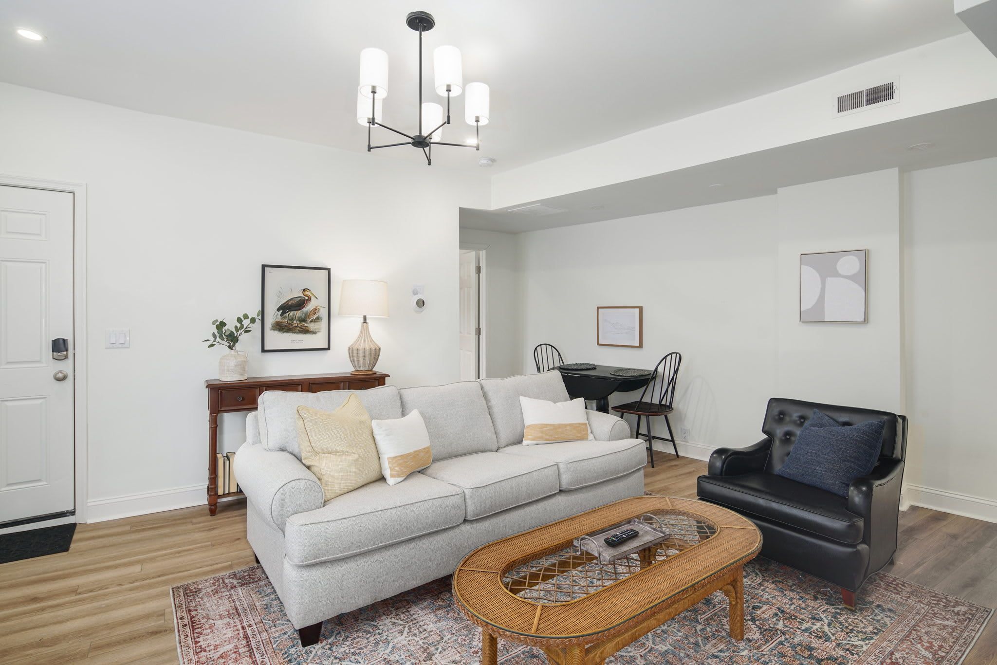 A living room with a sofa, a black leather chair, a coffee table, and a chandelier.