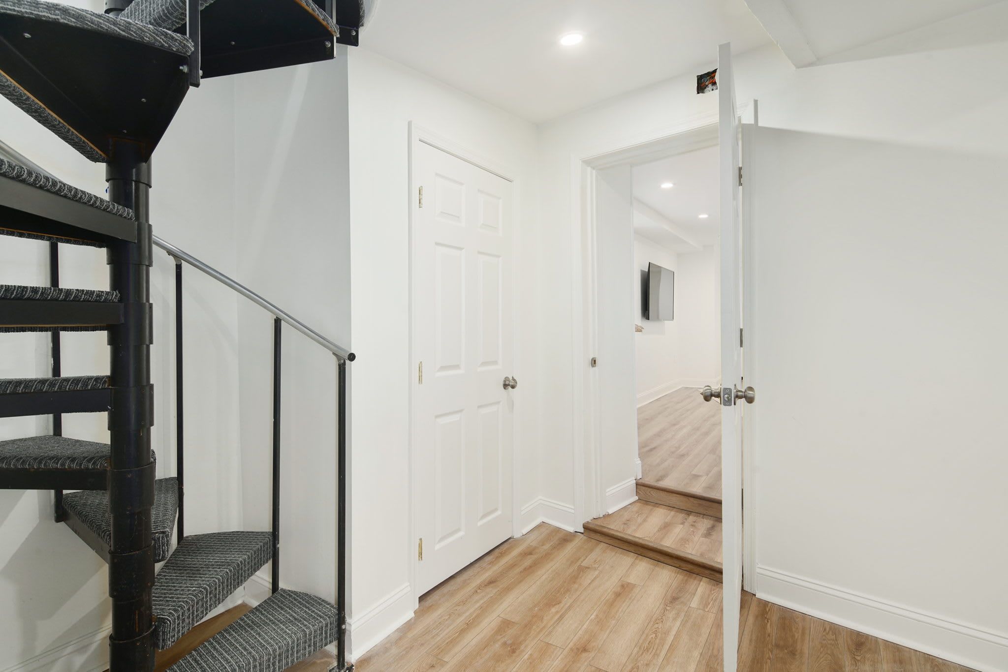A staircase with a handrail leading to a landing, a white door, and a hallway with wooden flooring.