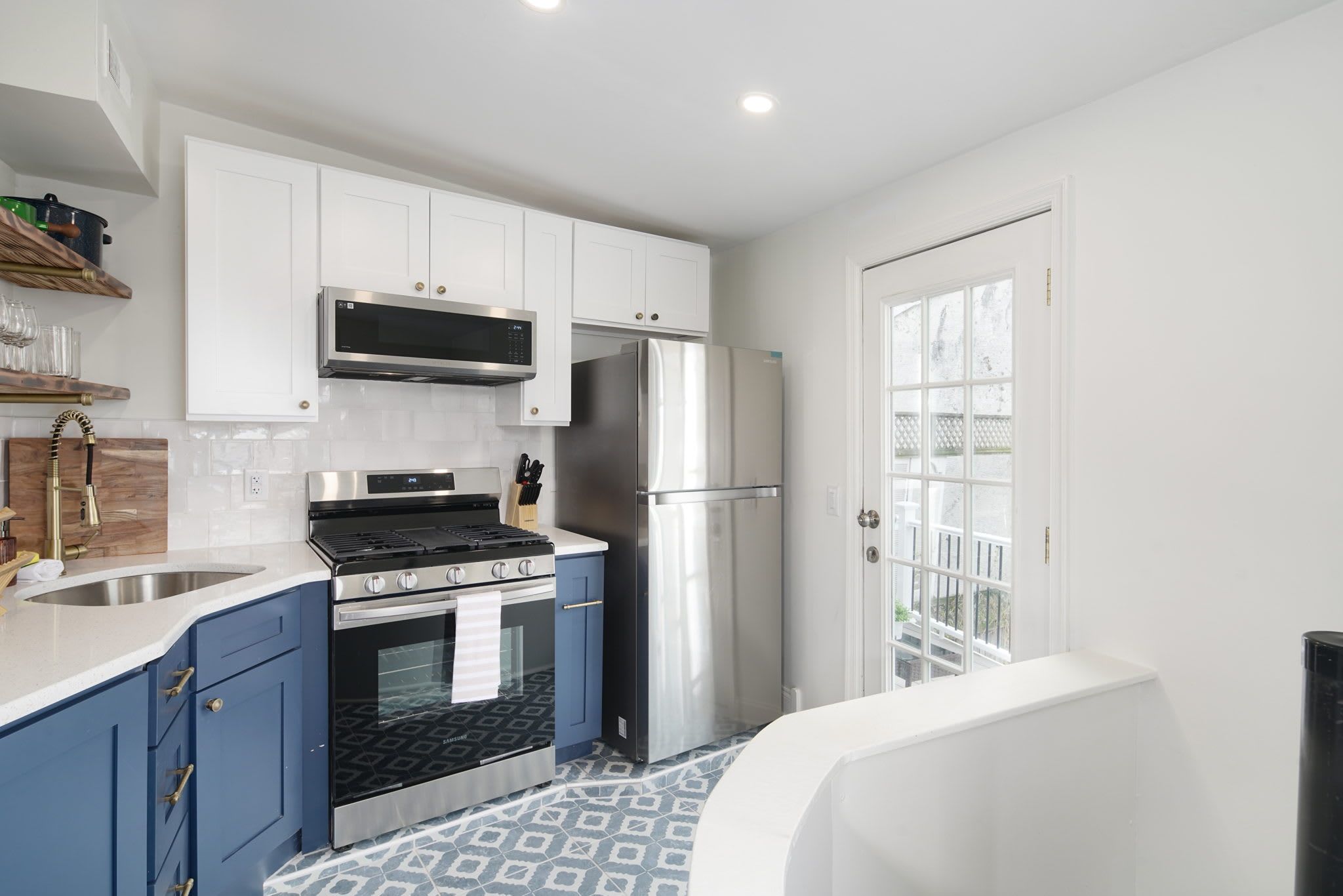 A modern kitchen with white cabinets, stainless steel appliances, and a patterned floor.