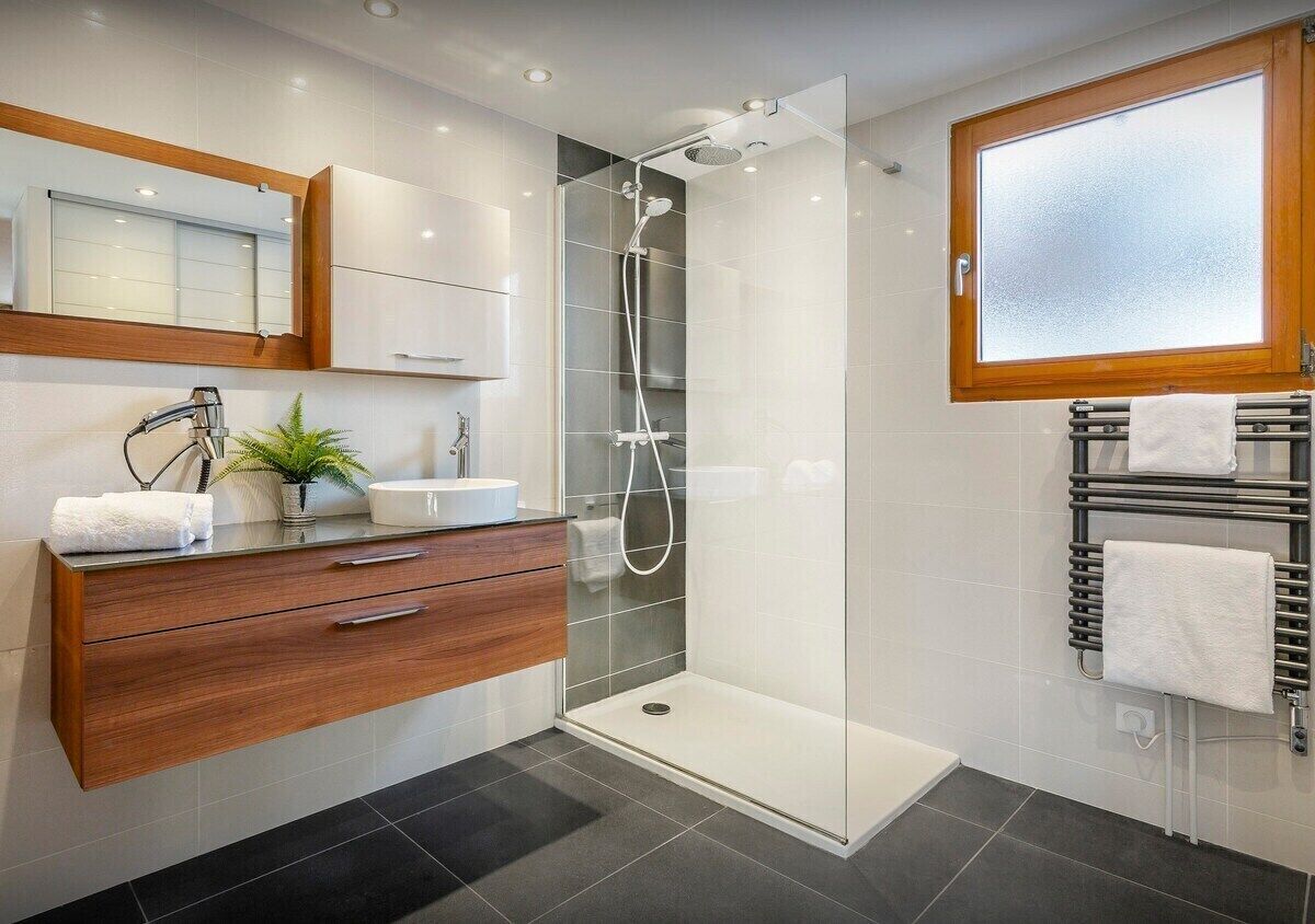A modern bathroom with a glass shower enclosure, a wooden vanity, a sink, and a towel rack.