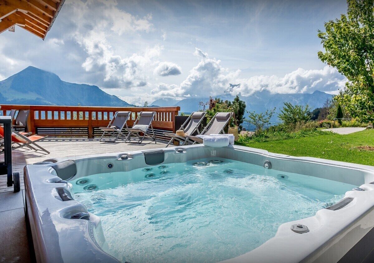 A hot tub with lounge chairs and a wooden deck overlooking a mountainous landscape.