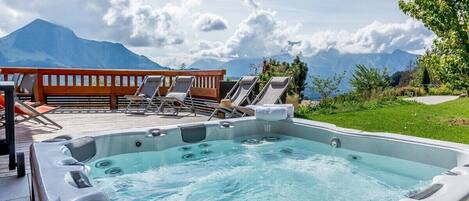 A hot tub with lounge chairs and a wooden deck overlooking a mountainous landscape.