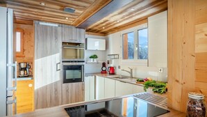 Eine moderne Küche mit Holzschränken, einem eingebauten Backofen, einer Kaffeemaschine und einem großen Fenster.
