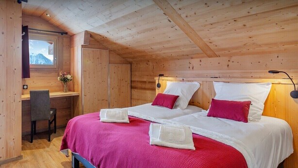 Ein Schlafzimmer in einer Holzhütte mit zwei Betten, einem Schreibtisch und einem Fenster mit Bergblick.