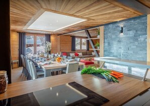 A modern dining area with a wooden ceiling, a stone wall, and a dining table set with chairs.