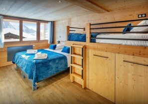 Une chambre avec un lit superposé, un bureau et une fenêtre donnant sur la montagne.