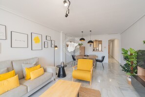 A modern living room with a sofa, armchairs, a coffee table, and a dining area with chairs and a table.