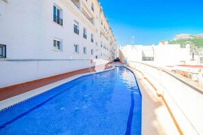 A swimming pool adjacent to a white building with multiple windows and balconies.