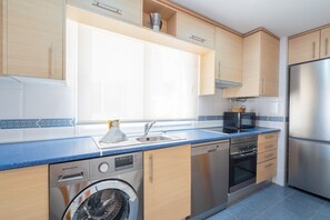 A modern kitchen with wooden cabinets, a stainless steel refrigerator, a dishwasher, and a washing machine.
