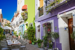 A narrow street with outdoor seating and potted plants.