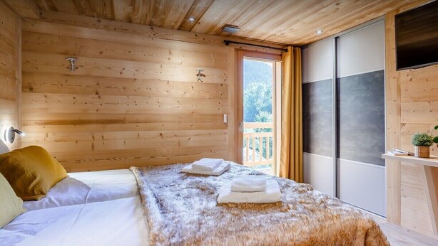 A wooden-paneled room with a bed, a window, and a sliding door.
