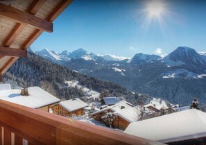 A wooden cabin with a snow-covered roof, surrounded by a mountainous landscape and a clear sky.
