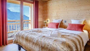 A wooden cabin bedroom with two beds, a balcony, and a mountain view.