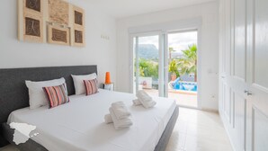 Ein Schlafzimmer mit einem großen Bett, einem Nachttisch und Blick auf einen Swimmingpool.