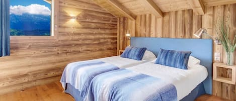 Une chambre à coucher dans un chalet en bois, avec un grand lit, une table de chevet, une lampe et une fenêtre donnant sur les montagnes.