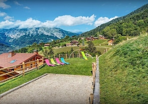 A mountainous landscape with wooden chalets, a grassy area with colorful chairs, and a clear sky.