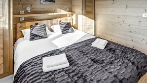 Habitació de fusta amb un llit, una tauleta de nit i una làmpada de paret.
