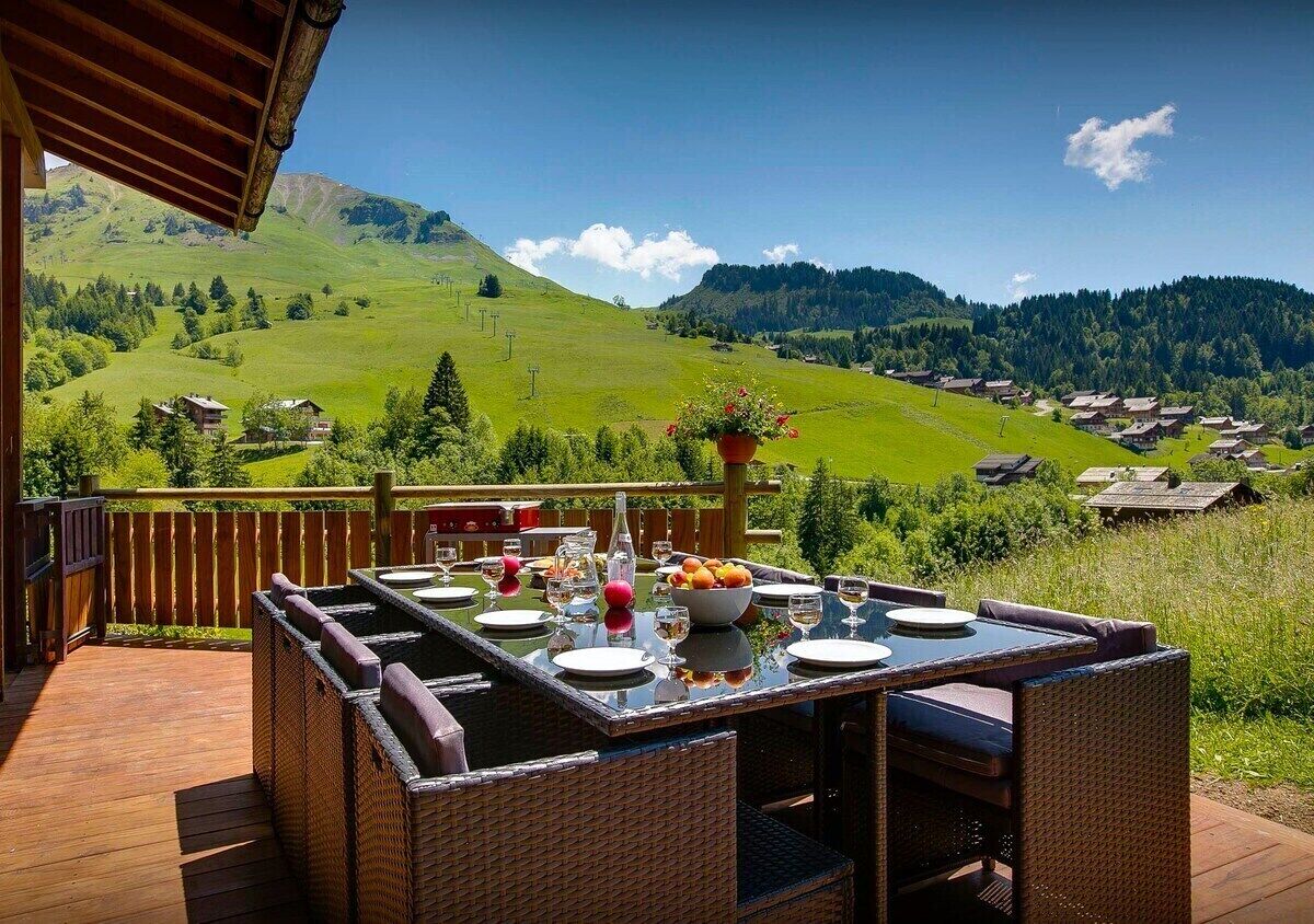 Un área de comedor al aire libre con una mesa dispuesta para cuatro personas, con vistas a un paisaje montañoso.