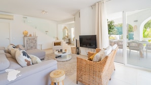 Ein modernes Wohnzimmer mit Sofa, Korbsessel, Fernseher und Essbereich mit Außensitzgelegenheiten.