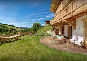 A wooden deck with a hot tub, lounge chairs, and a hammock.