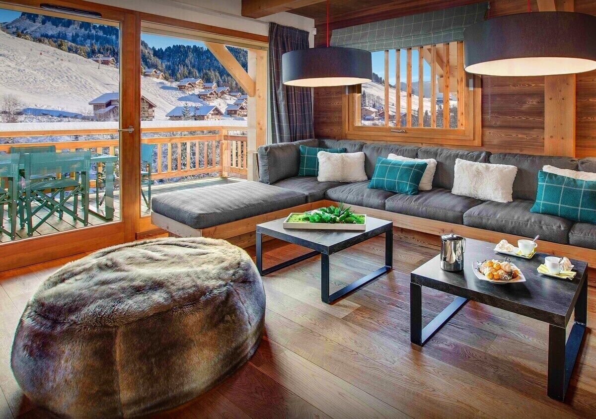 A modern living room with a sofa set, ottoman, and coffee table, featuring a view of a snowy mountain landscape.