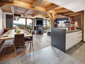 Une cuisine moderne dotée d’un îlot central, de poutres en bois, d’un coin repas avec une longue table et d’une cheminée.