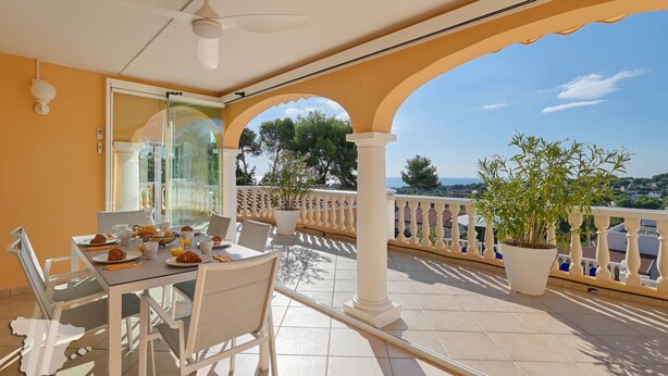 A balcony with a table set for breakfast, a potted plant, and a view of the landscape.