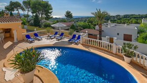 A swimming pool with blue water, surrounded by a white fence and blue lounge chairs.