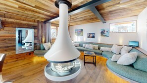 A cozy living room with a large, modern fireplace, a green sofa, and a wooden ceiling. - Ski base piste views, 14 people, pool and sauna (Le Grand-Bornand)