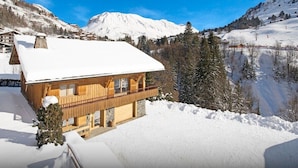 A wooden chalet with a balcony, surrounded by snow-covered mountains and trees. - Ski base piste views, 14 people, pool and sauna (Le Grand-Bornand)