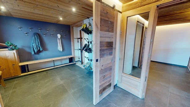A room with a wooden bench, a wall-mounted coat rack, and a wooden door with a mirror. - Ski base piste views, 14 people, pool and sauna (Le Grand-Bornand)