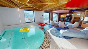 A spacious indoor area with a large pool, seating area, and wooden ceiling.