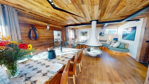 A cozy interior with a wooden ceiling, a dining area with a table set for two, a sofa, and a fireplace. - Ski base piste views, 14 people, pool and sauna (Le Grand-Bornand)