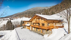A wooden chalet with a balcony, surrounded by snow-covered landscape and mountains. - Luxury chalet with swimming pool and jacuzzi (Manigod)