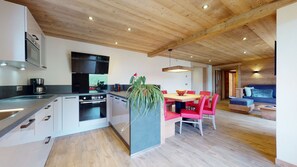 A modern kitchen with a central island, a dining area with red chairs, and a cozy living space with a sofa. - Magnificent T4 in a renovated traditional chalet (Le Grand-Bornand)
