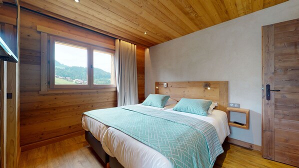 Une chambre à coucher aux murs lambrissés, avec un lit, une table de chevet et une fenêtre donnant sur l’extérieur.