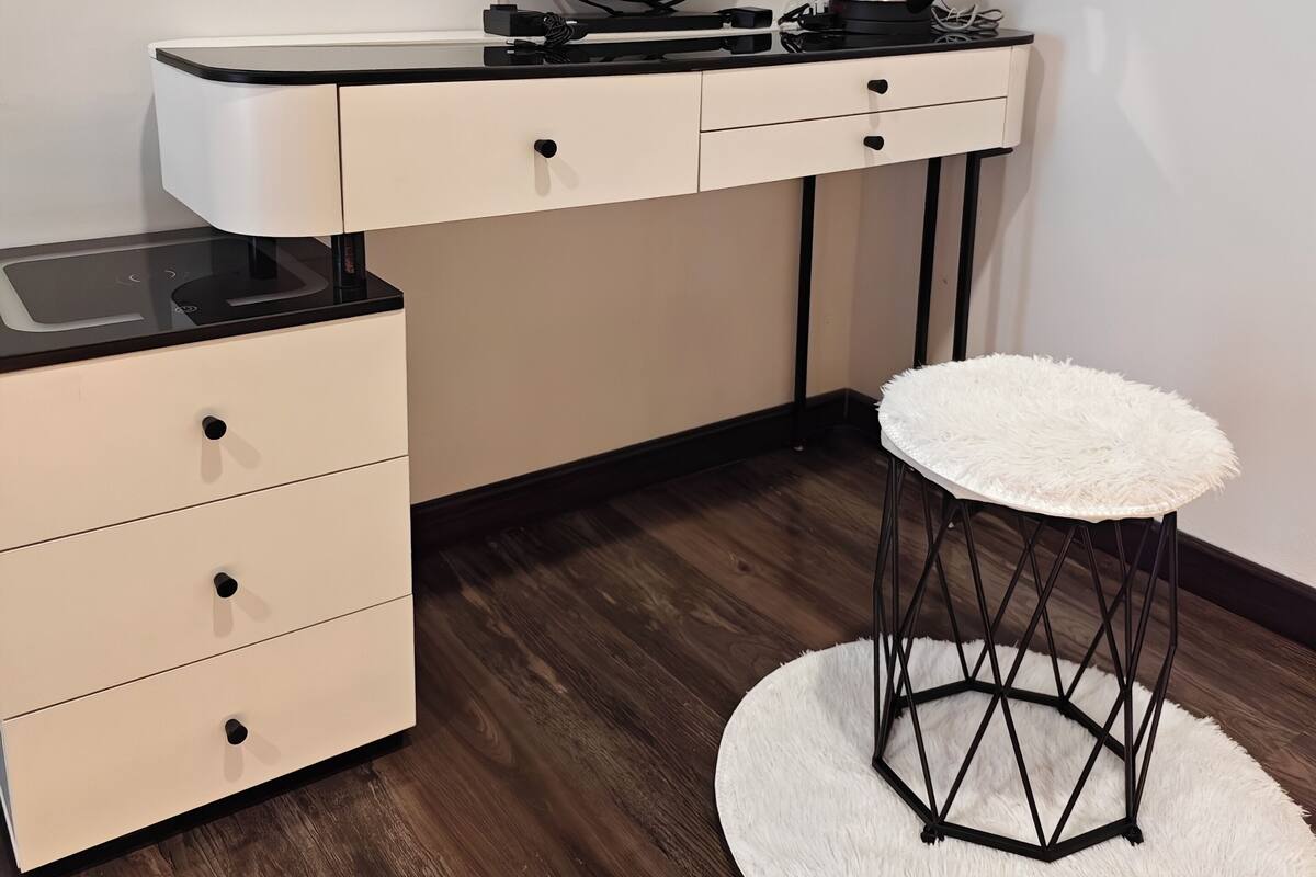 A modern vanity with a round mirror, a black kettle, and a white fluffy stool.