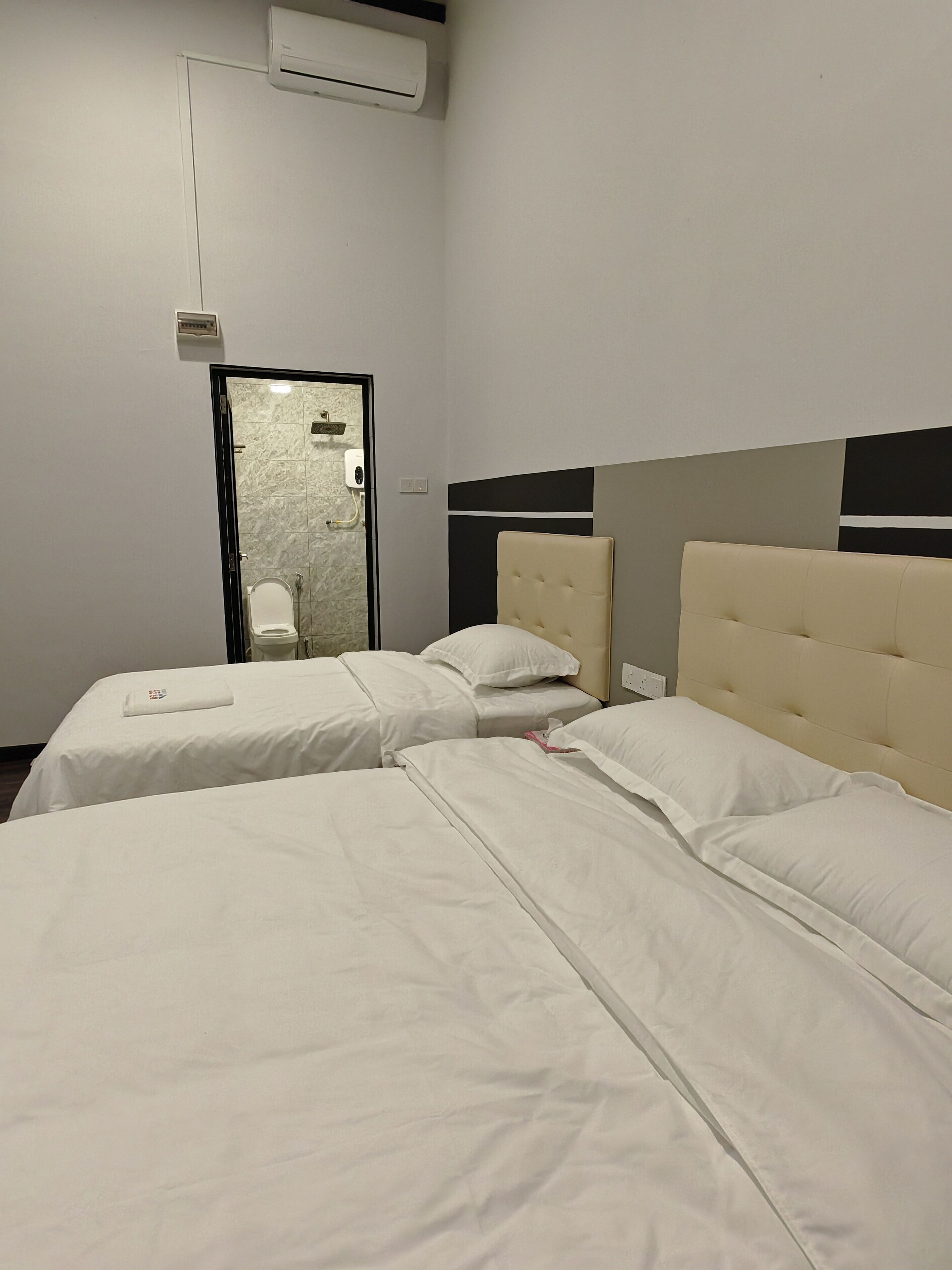 A hotel room with two beds, a bathroom with a shower, and an air conditioning unit.